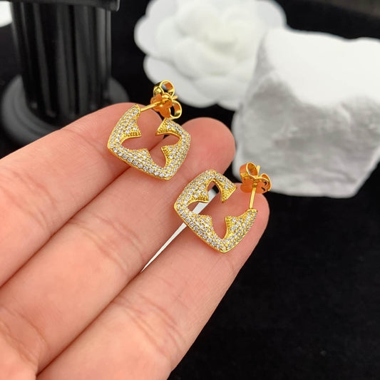 Gold earrings with diamond accents held in a hand against a dark background
