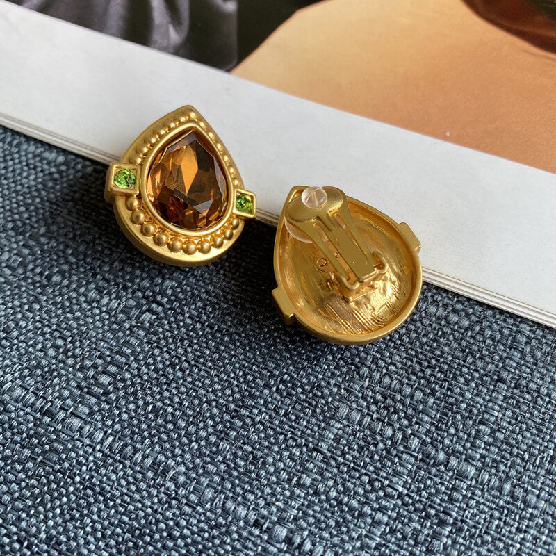 Gold earrings with a central gemstone on a textured surface