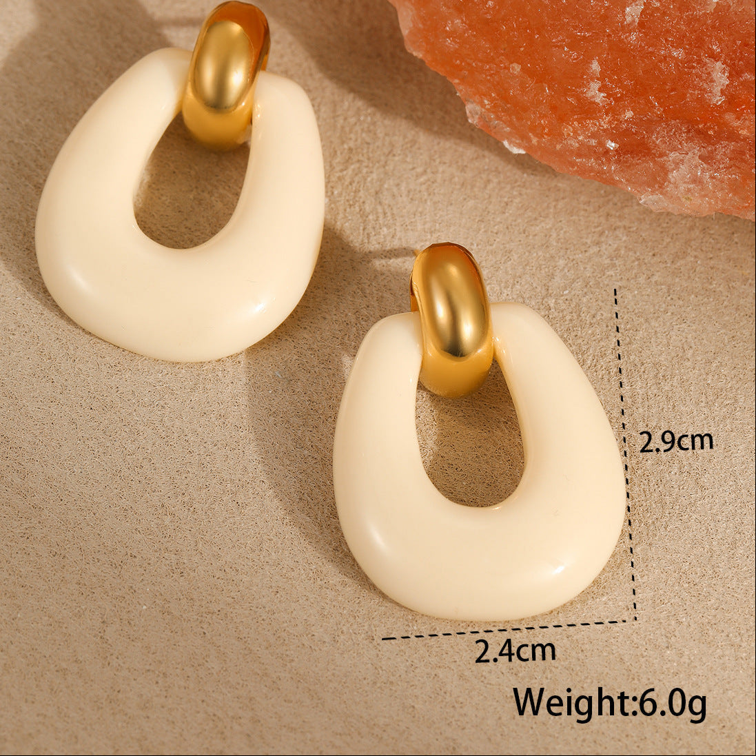 Pair of earrings with gold and white design on a textured surface with measurements and weight displayed.