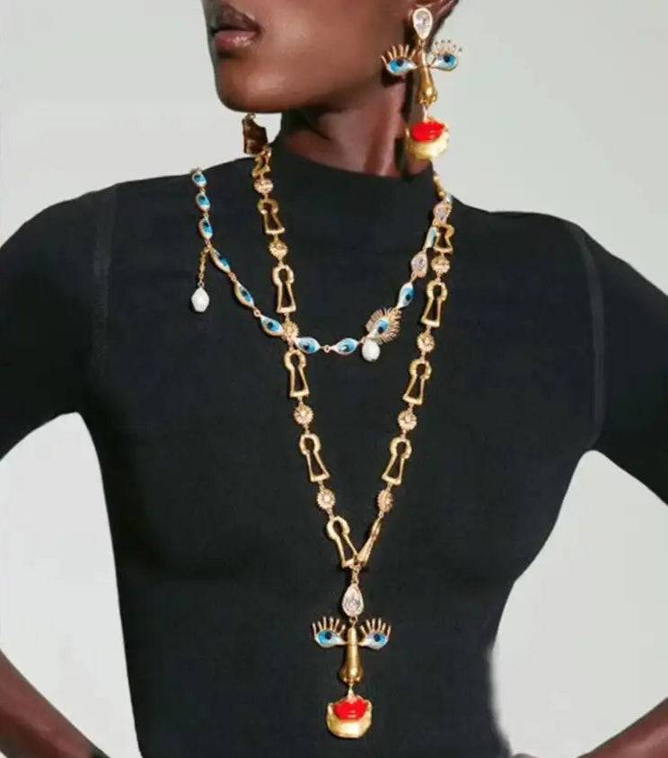Person wearing a long, ornate necklace with intricate designs on a plain background