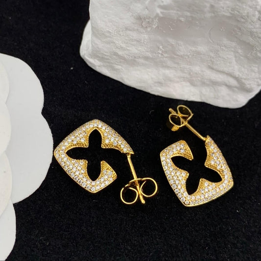 Gold earrings with black center design on a black background with white flowers.
