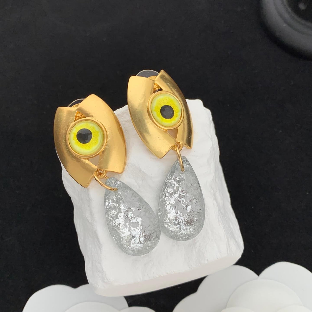 Gold and silver eye-shaped earrings on a white stone surface with a black background