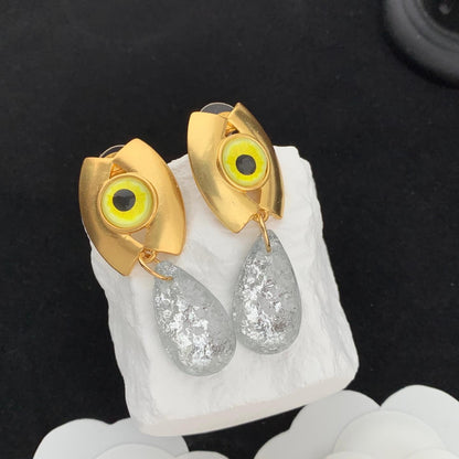 Gold and silver eye-shaped earrings on a white stone surface with a black background