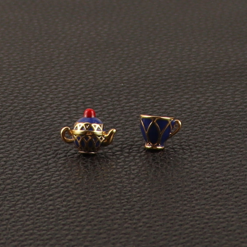 Teapot and teacup-shaped charms on a textured black surface