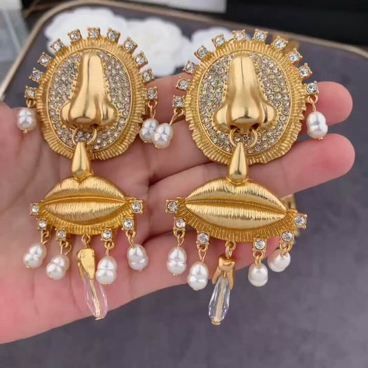 Gold earrings with pearl accents held in a hand against a neutral background