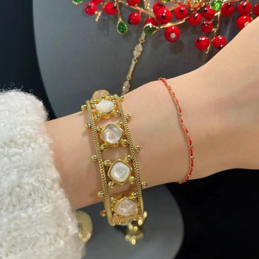 Gold bracelet with red beads on a wrist against a dark background