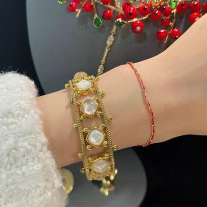Gold bracelet with red beads on a wrist against a dark background