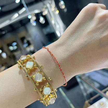 Gold bracelet with stone accents on a wrist against a blurred indoor background