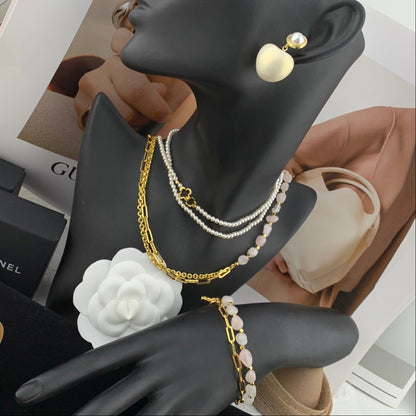 Black mannequin hand with jewelry including a gold chain, pearl bracelet, and earrings on a blurred background.