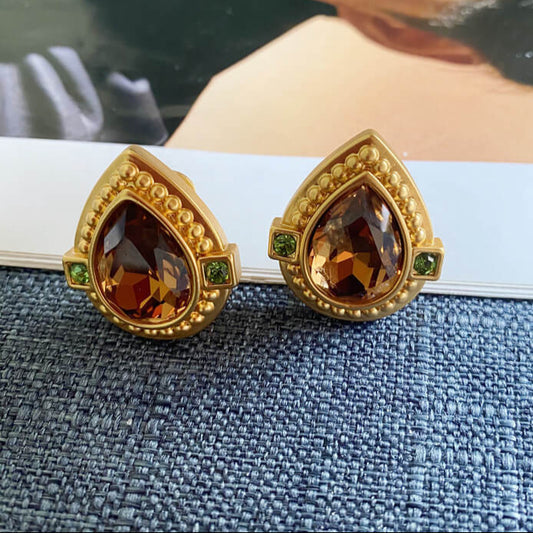 Gold earrings with teardrop-shaped gemstones on a textured surface