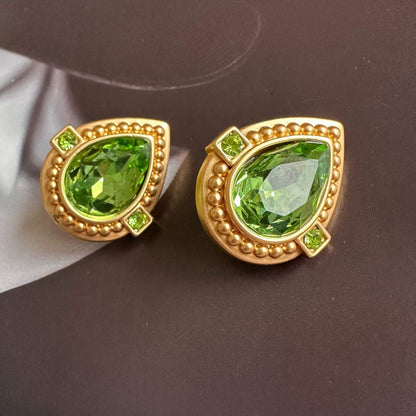 Gold earrings with green gemstones on a dark surface