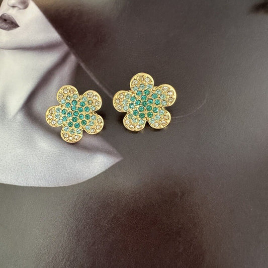 Gold flower-shaped earrings with green gemstones on a dark background
