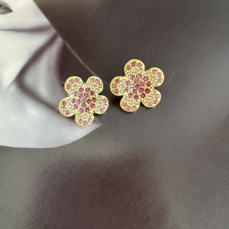 Gold flower-shaped earrings with pink gemstones on a gray background