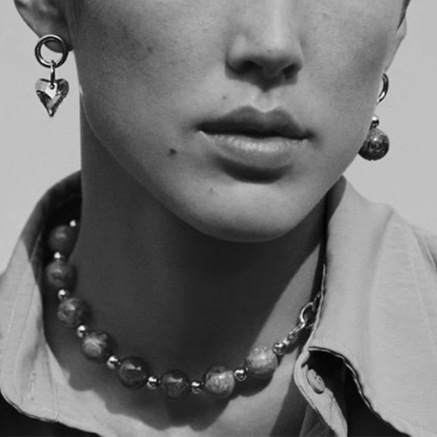 Close-up of a person wearing a necklace and earrings with a neutral background