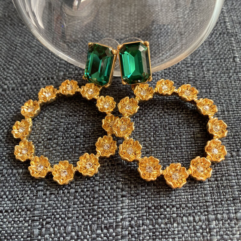 Gold earrings with green gemstones on a textured gray surface