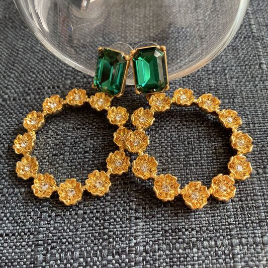 Gold earrings with green gemstones on a textured gray surface