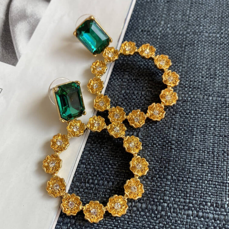 Gold earrings with green gemstones on a textured surface