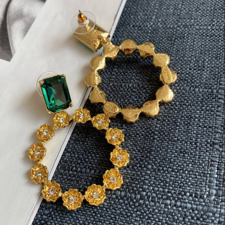Gold hoop earrings with green gemstone on a textured surface