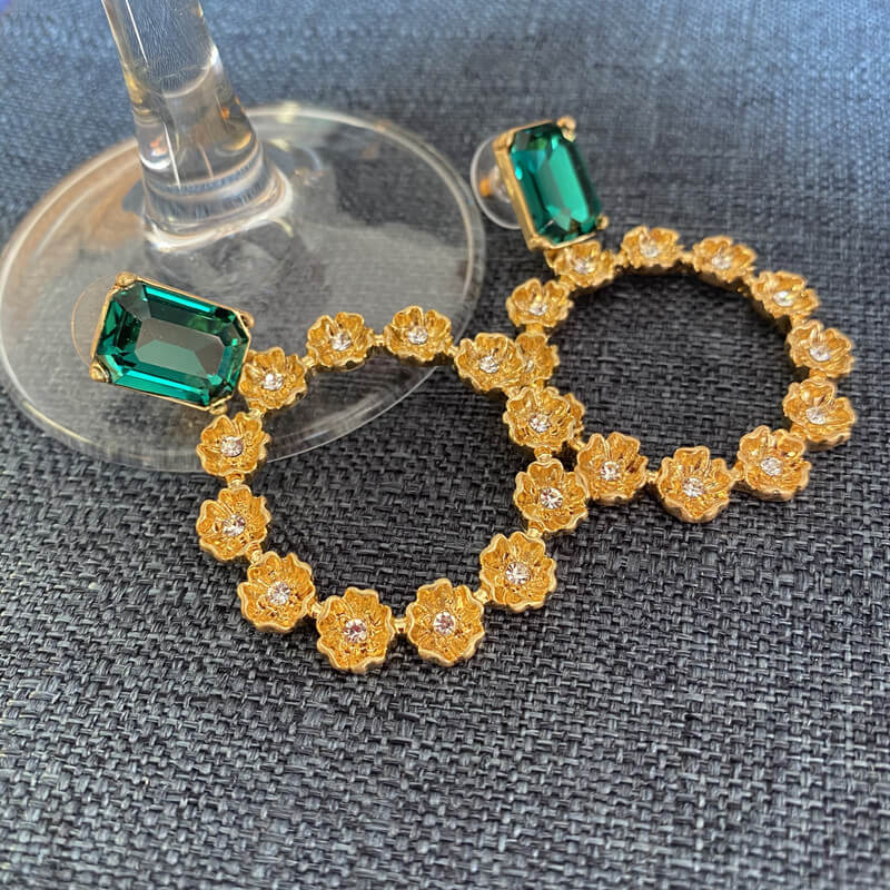 Gold hoop earrings with green gemstones on a gray surface