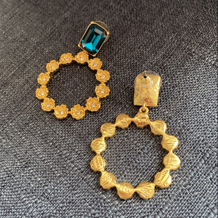Gold hoop earrings with a blue gemstone on a gray textured background