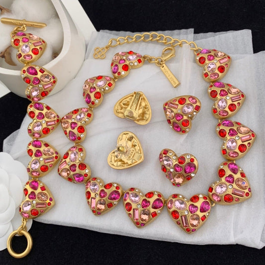 Gold necklace with heart-shaped pink and red gemstones on a white surface.