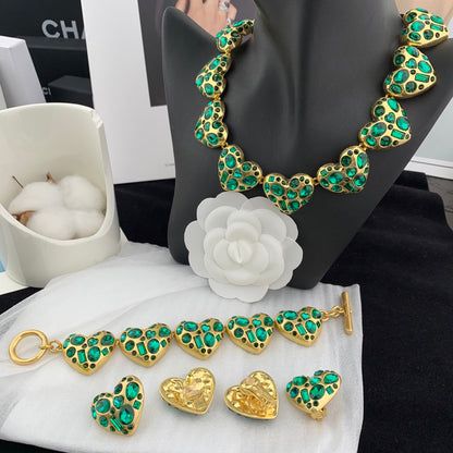 Gold and green jewelry set on a black stand with a white flower and white apples in the background.