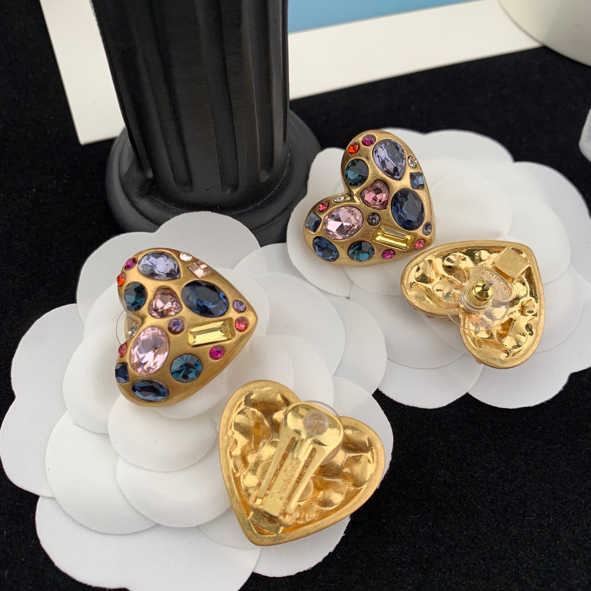 Heart-shaped earrings with gemstones on a white flower stand.
