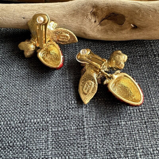 Pair of gold earrings on a textured gray surface with a wooden log in the background.