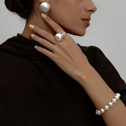Person wearing pearl earrings and bracelet on a plain background