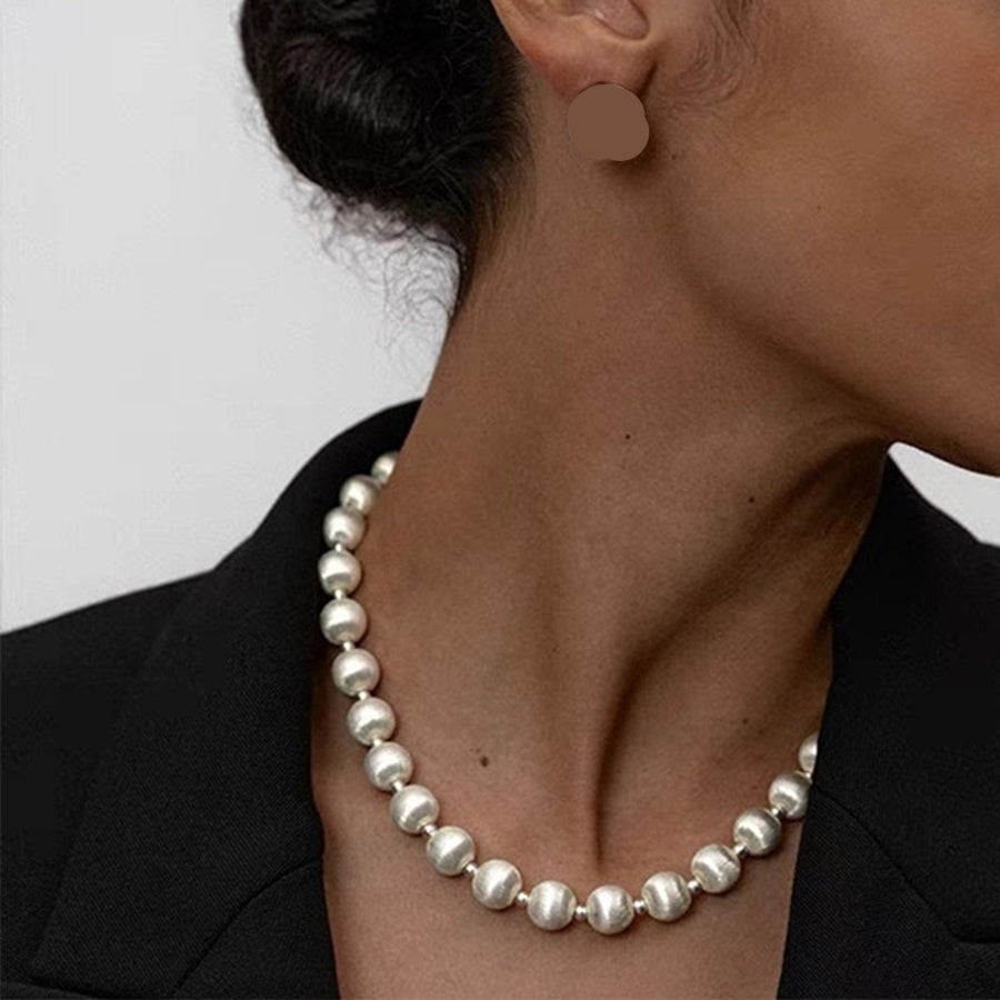 Pearl necklace and earrings on a person against a neutral background