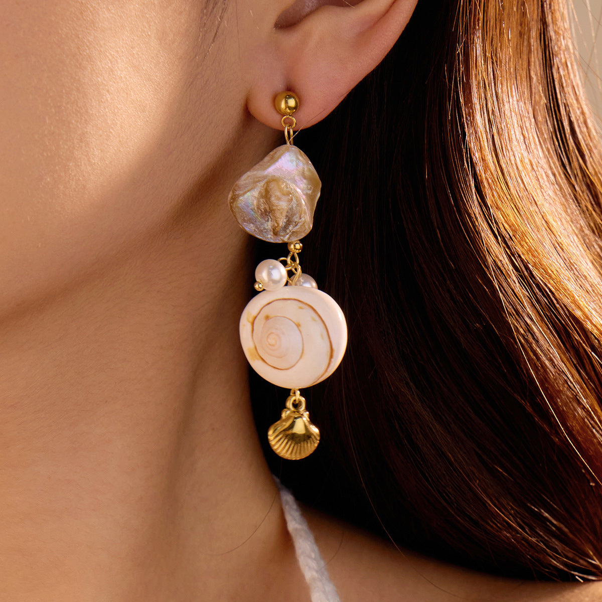 Close-up of a woman wearing elegant earrings with pearls and gold accents.