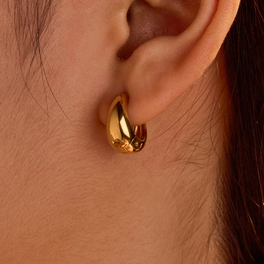 Gold hoop earring worn on an ear with a close-up view.