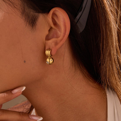 Close-up of a person wearing gold hoop earrings with a neutral background