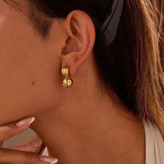 Close-up of a person wearing gold hoop earrings with a neutral background