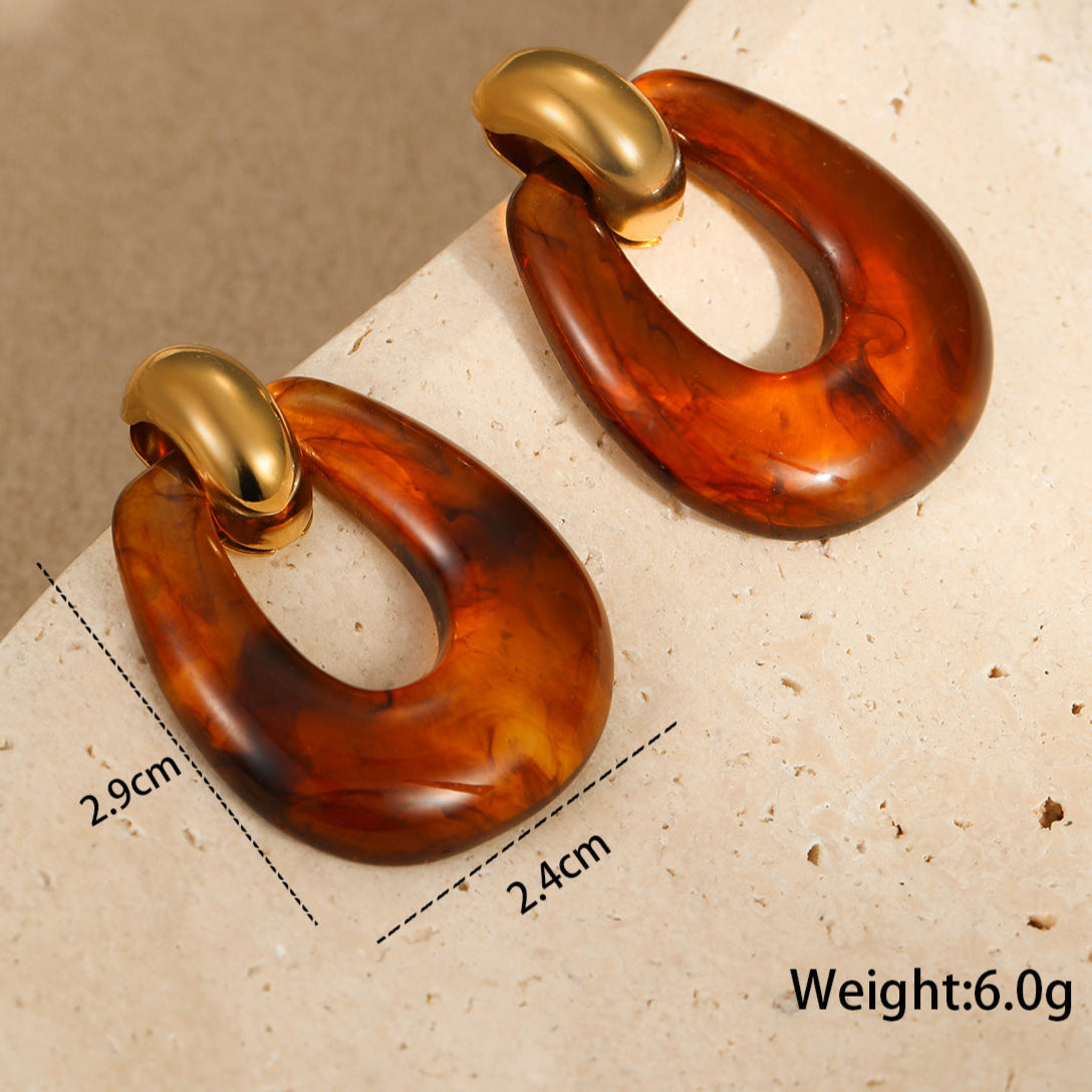 Pair of amber-colored earrings with gold accents on a beige surface, showing measurements and weight.