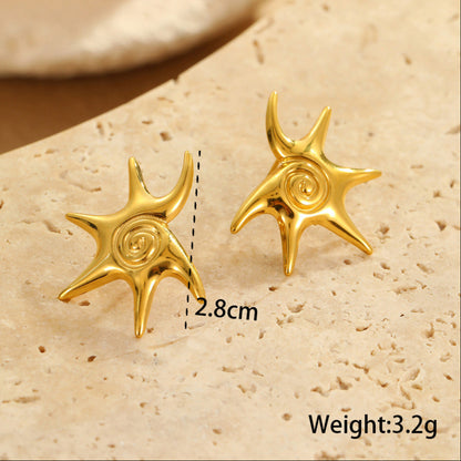 Gold star-shaped earrings on a beige stone surface with measurements and weight displayed.