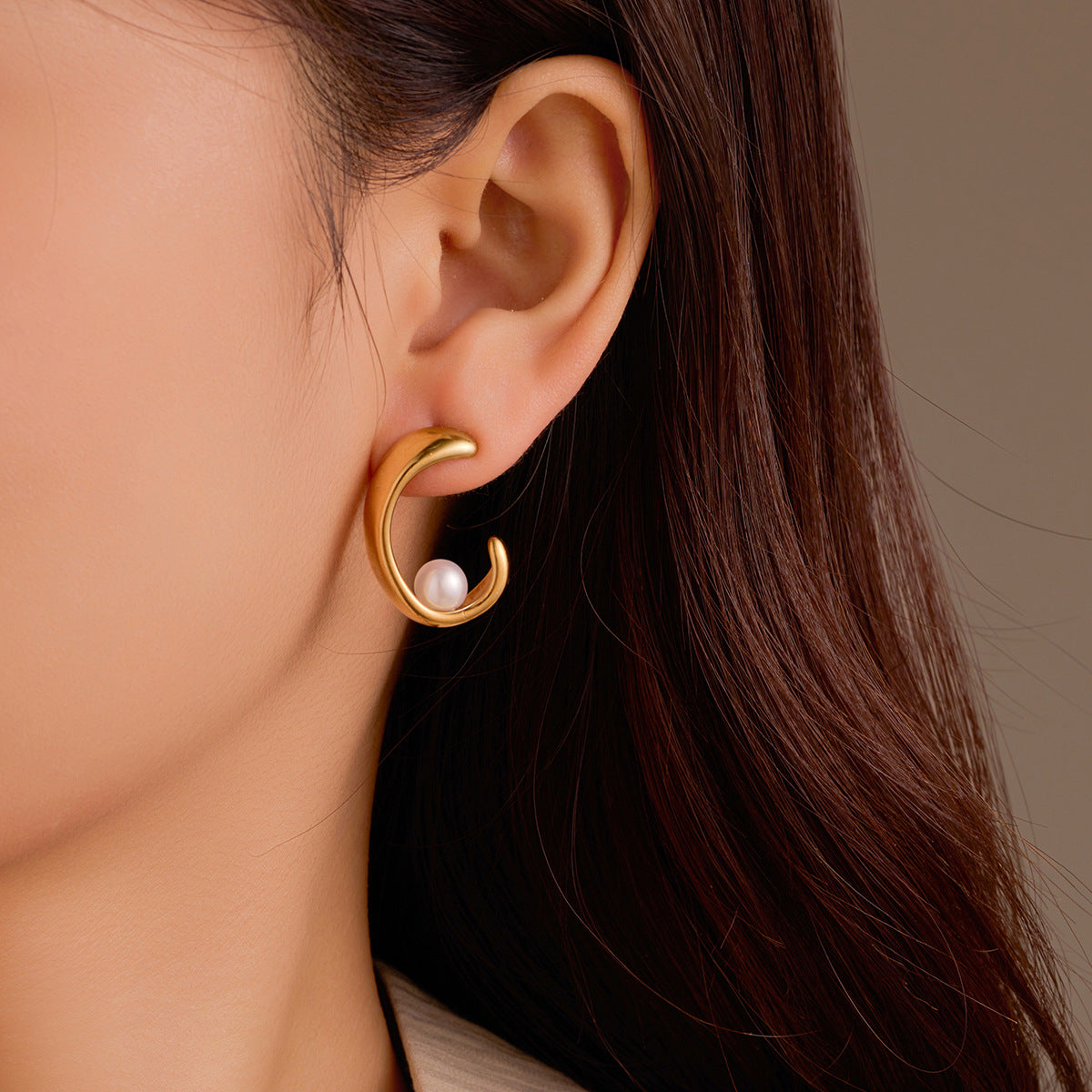 Gold earring with a pearl on an ear against a neutral background