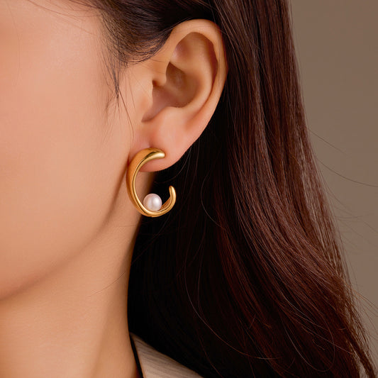 Gold earring with a pearl on an ear against a neutral background