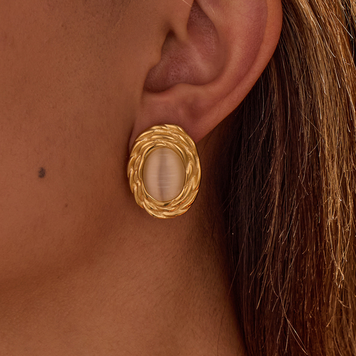 Gold earring worn on an ear with a close-up view
