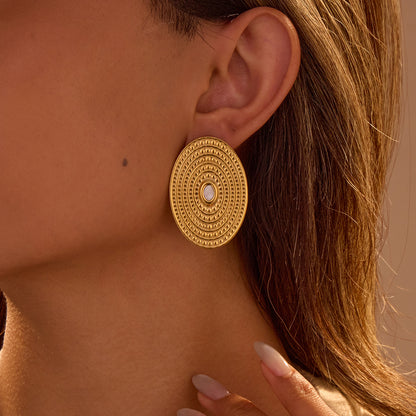 Gold earrings worn by a person with a neutral background