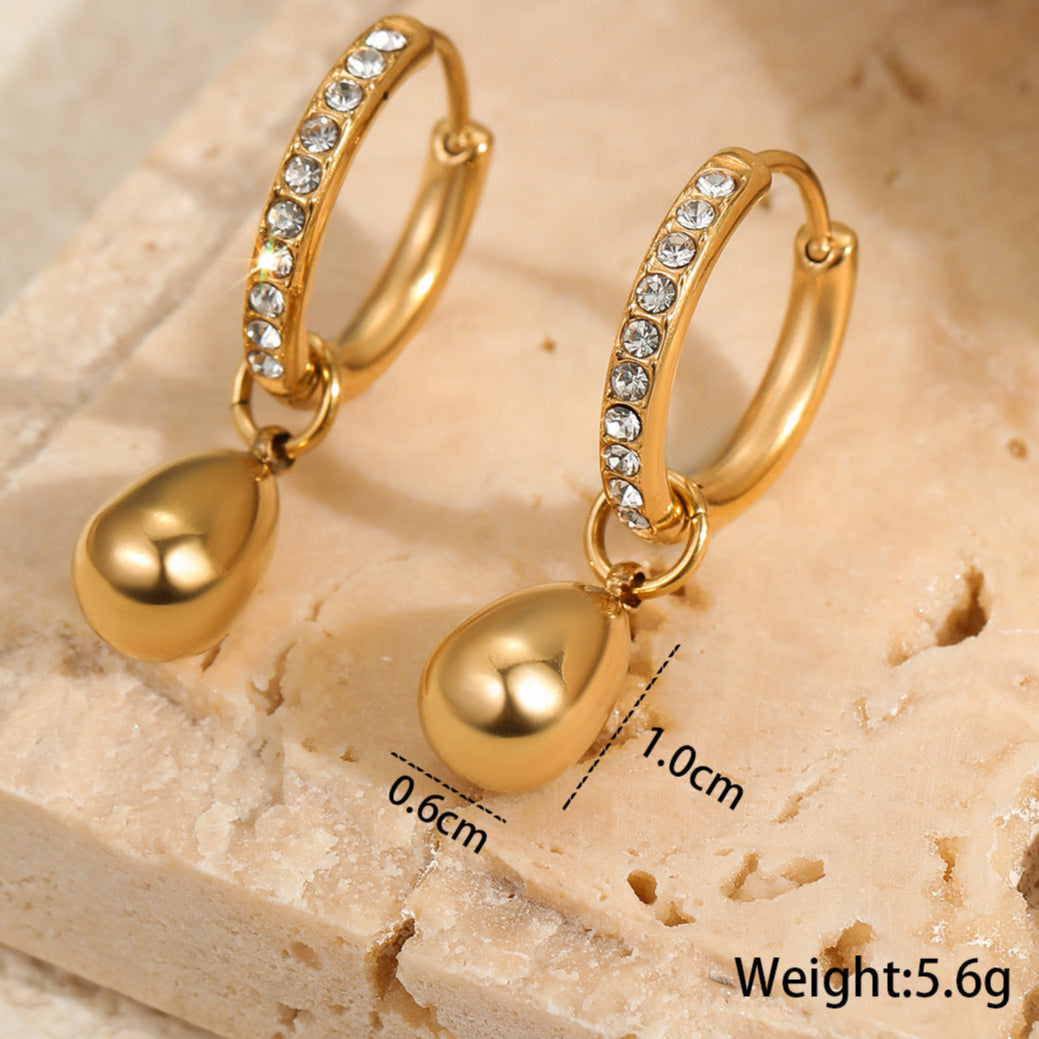 Gold hoop earrings with teardrop pendants on a textured beige surface, showing measurements and weight.