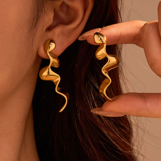 Gold earrings being worn and adjusted by a hand against a neutral background