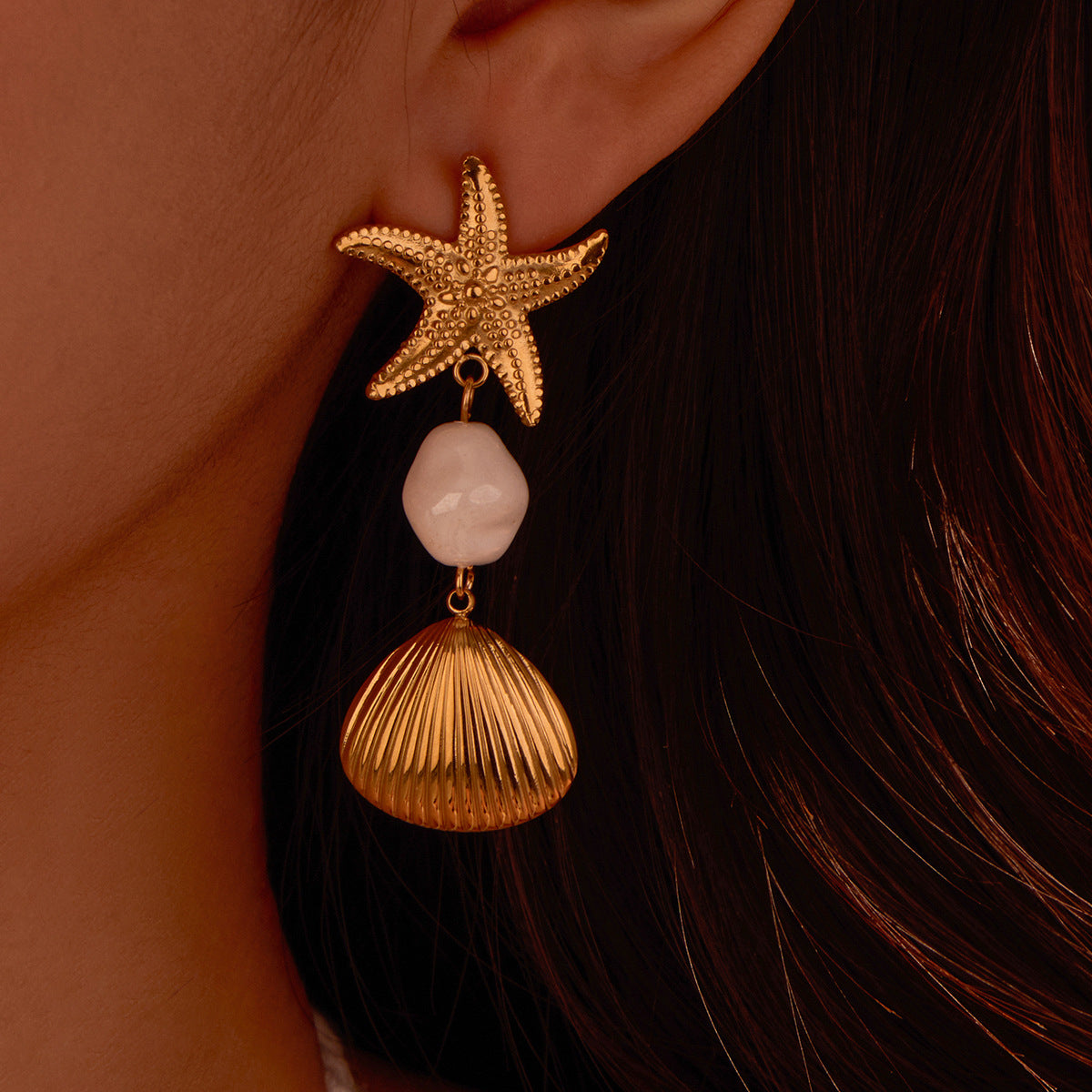 Gold starfish and shell earring on a person's ear with a blurred background