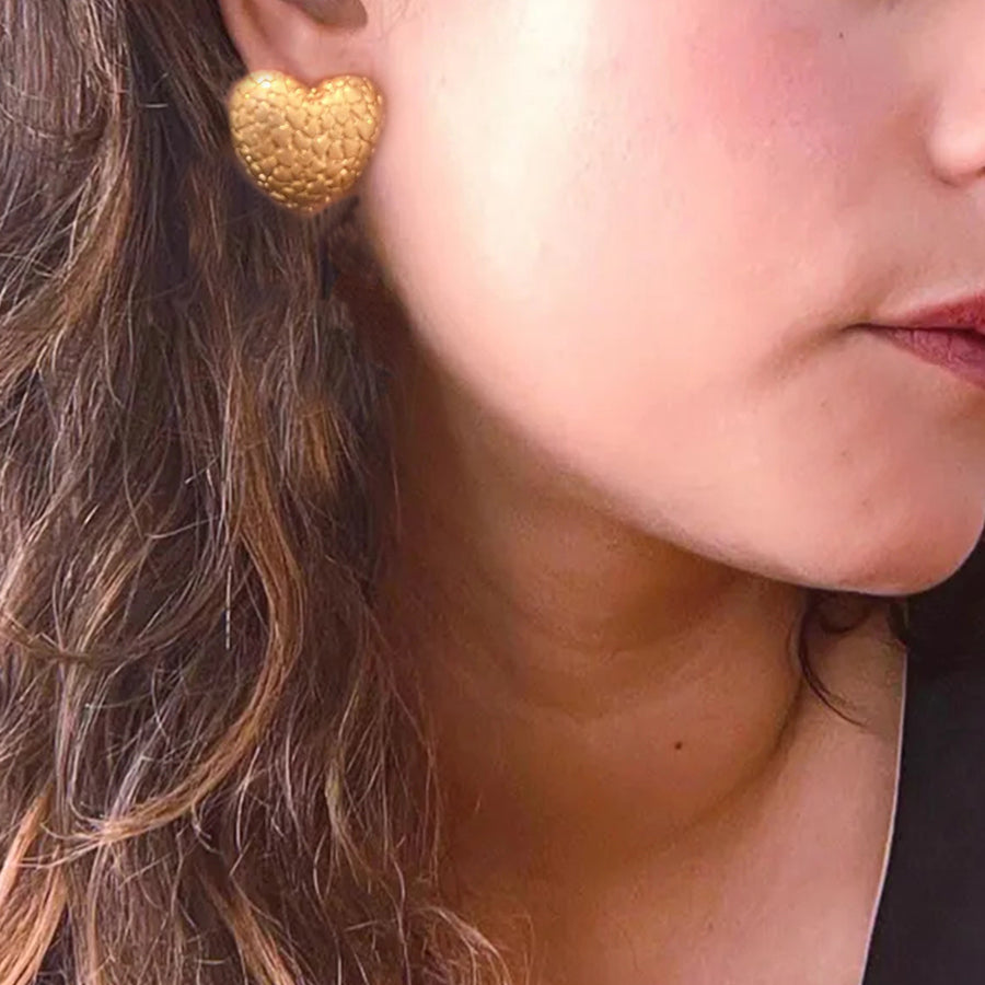 Close-up of a person wearing a gold heart-shaped earring.