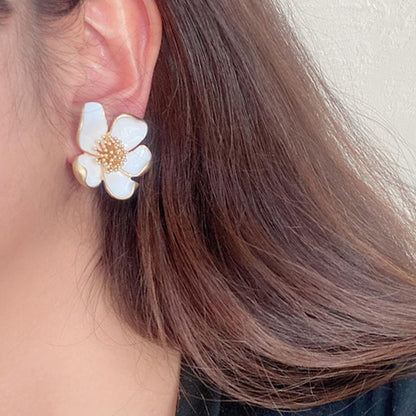 a person wearing a white flower-shaped earring with gold accents.
