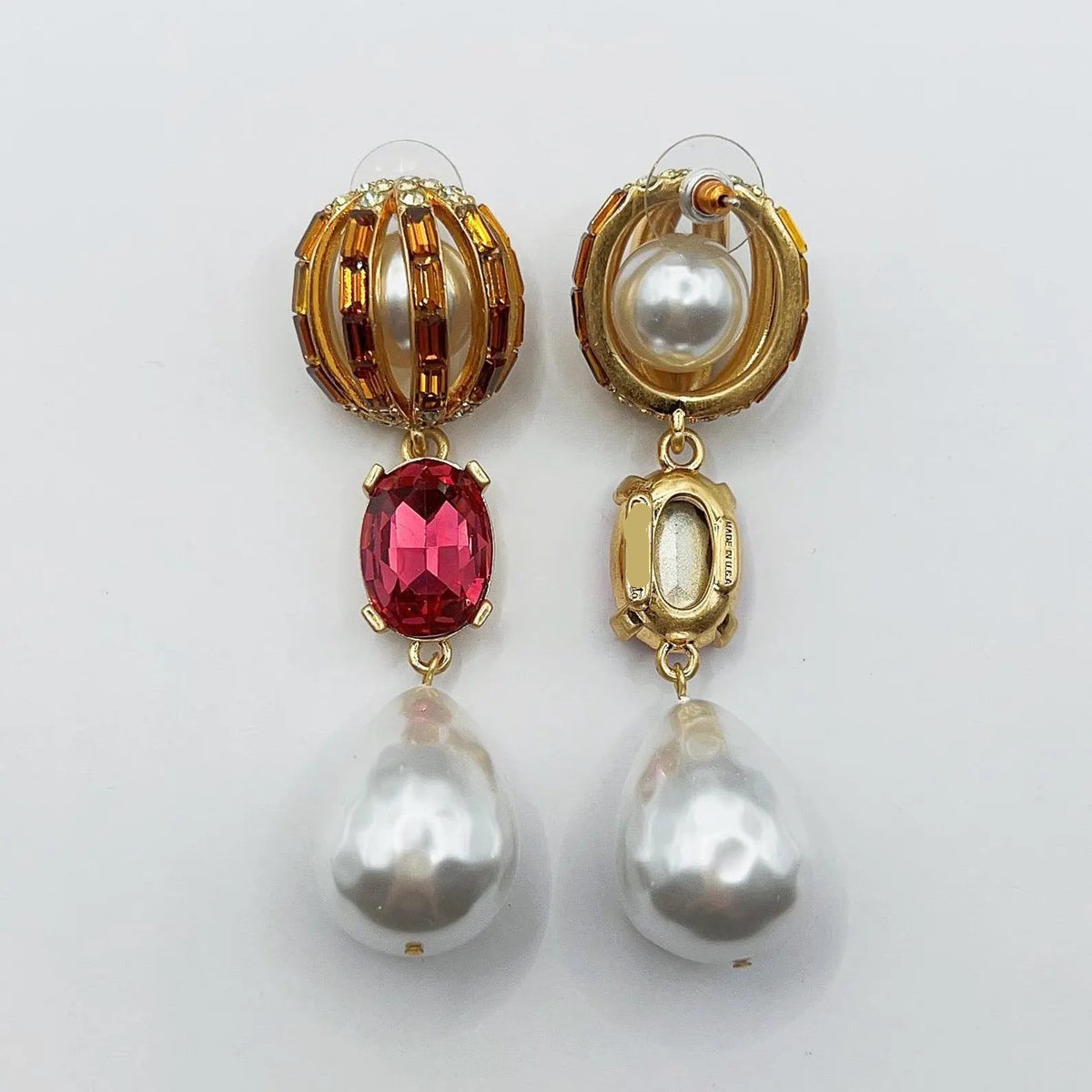 Pair of earrings with gold, red gemstone, and pearl elements on a white background