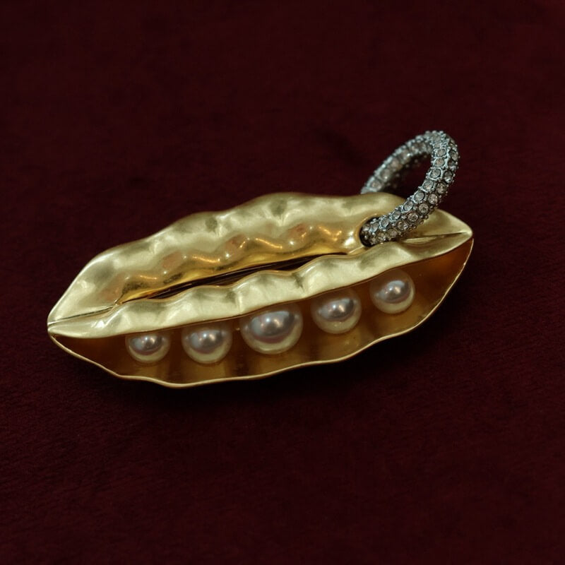 Gold leaf-shaped brooch with pearls and a diamond-studded band on a dark red background