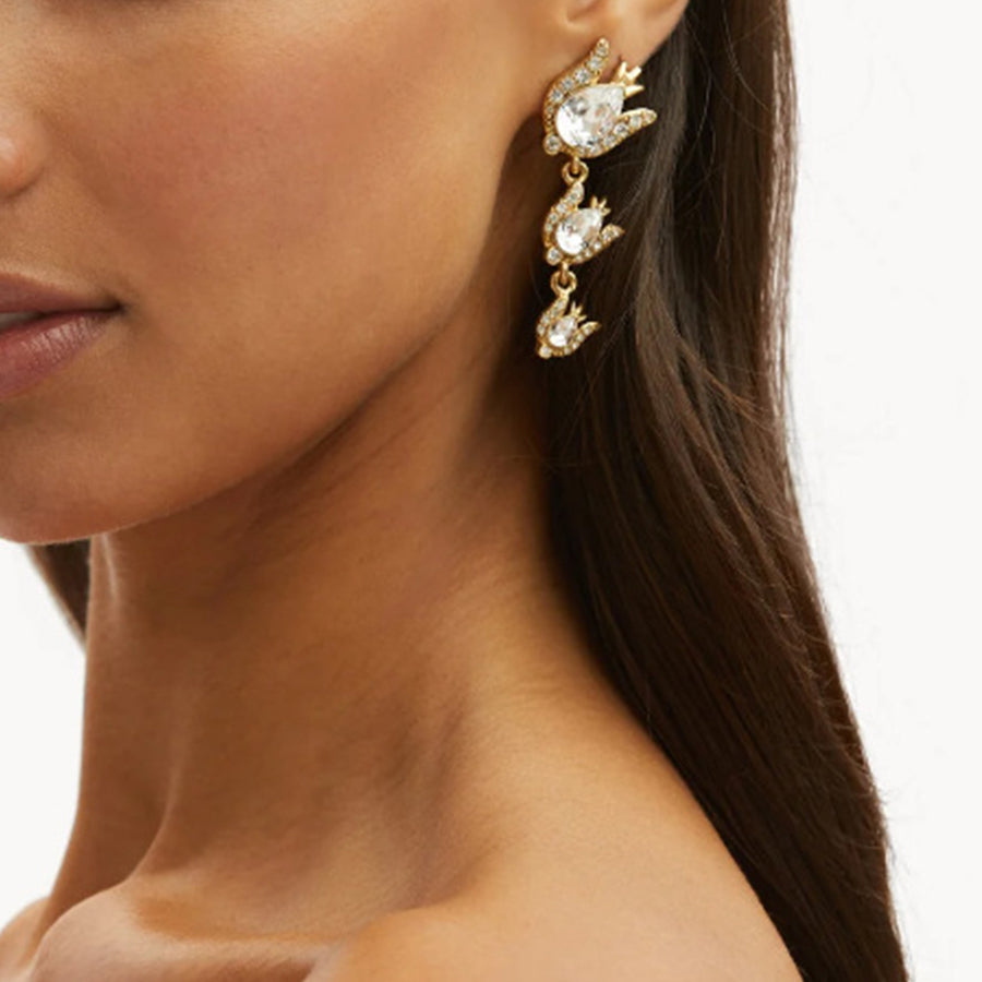 Close-up of a woman wearing gold earrings with clear stones on a white background