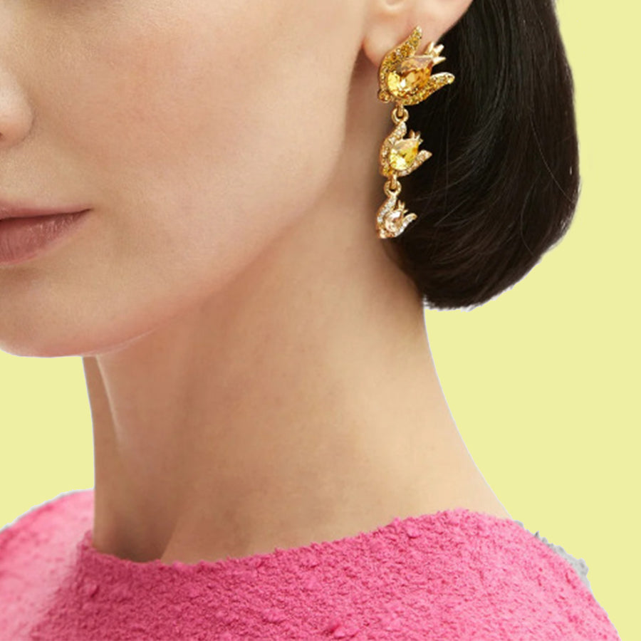 Close-up of a person wearing gold earrings with yellow gemstones against a green background