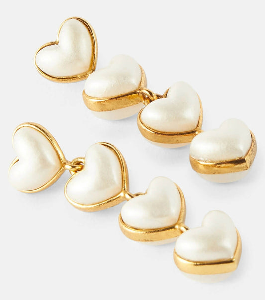 Heart-shaped earrings with gold and white finish on a light gray background